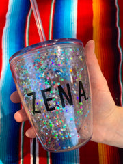 the Zena sparkly cup close up with a hand around it to show the size. Colourful background