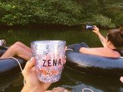 The Zena glitter cup photographed in a disposable camera feel in front of a scene with friends tubing down the  river Nile having fun and taking photos. 